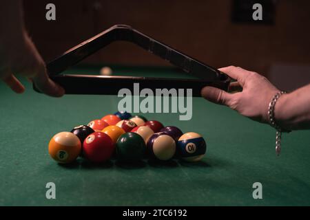 Le mani maschili preparano la partita sportiva del biliardo su un panno verde. Palline da biliardo multicolore in triangolo con numeri Foto Stock