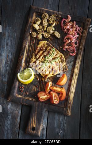 Bistecca di manzo con funghi e pomodori su un piatto di legno sopra Foto Stock