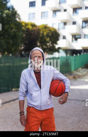 Uomo anziano che gioca a pallacanestro all'aperto su un campo da pallacanestro in città. L'uomo più anziano e vitale ha uno stile di vita attivo, fa sport ogni giorno. Foto Stock