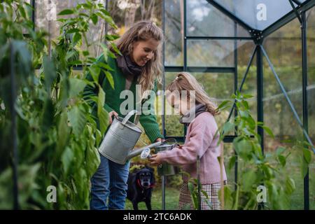 Bambina e madre che annaffiano le piante in giardino, usando acqua piovana raccolta. Concetto di conservazione dell'acqua in giardino e giardinaggio familiare. Foto Stock