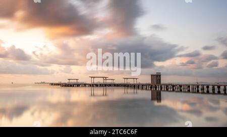 Alba su un molo di legno nel Mar Menor, nel sud della Spagna. Il mare è perfettamente fermo e riflette le nuvole e il molo Foto Stock