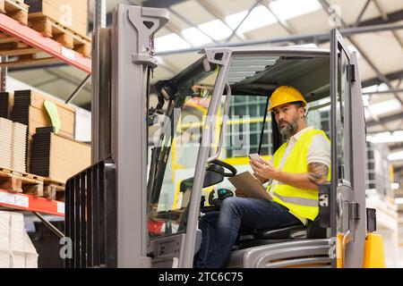 Driver carrello elevatore a forche magazzino che controlla l'ordine di spedizione. Addetto al magazzino che prepara i prodotti per il mennt, consegna, controllo delle scorte in magazzino, ordine Foto Stock