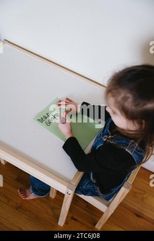 Una bambina seduta che scrive una lettera di natale a Babbo Natale Foto Stock