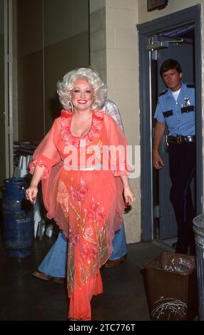 Durante il suo tour estivo del 1978, Dolly Parton lascia il suo spogliatoio e si dirige verso il palco sotto l'occhio vigile della sicurezza. sicurezza. Foto Stock