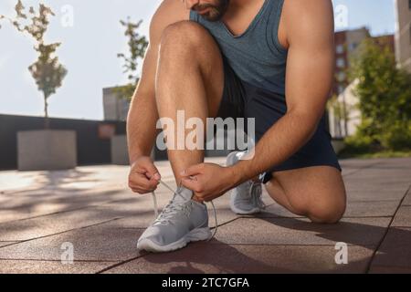 Uomo che stringe le scarpe prima di correre all'aperto nelle giornate di sole, primo piano Foto Stock