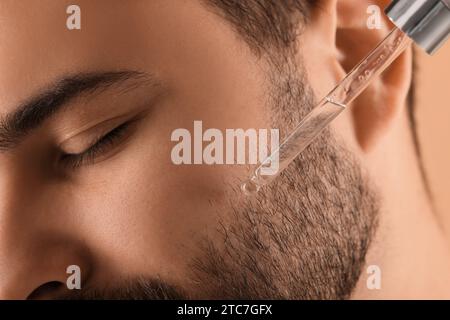 Uomo che applica siero cosmetico sul viso, primo piano Foto Stock