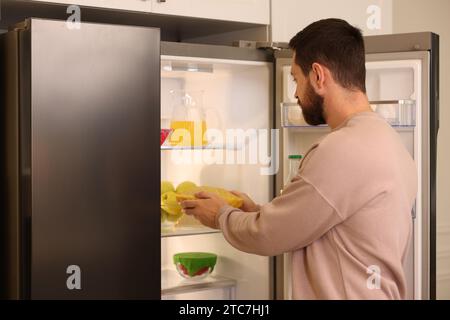 Uomo che mette la ciotola coperta da un involucro di cera d'api in frigorifero al chiuso Foto Stock