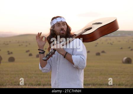 Elegante uomo hippie con fumante chitarra in campo Foto Stock