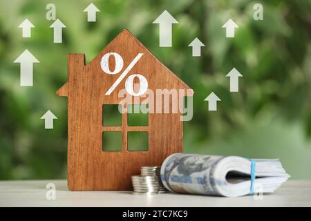 Aumento del tasso ipotecario illustrato da frecce verso l'alto e segno di percentuale. Modello di casa e denaro sul tavolo Foto Stock