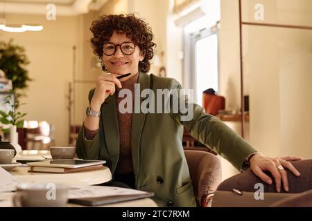 Foto media di una giovane donna caucasica che posa con sicurezza al tavolo in un bar sorridente davanti alla macchina fotografica Foto Stock