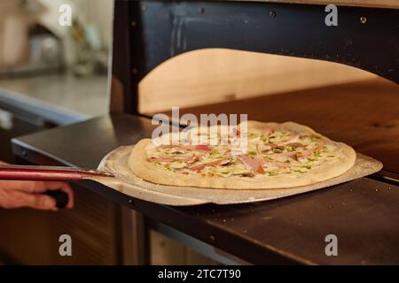 Primo piano della pizza pronta su una buccia di ferro da stiro che viene estratta direttamente dal forno Foto Stock