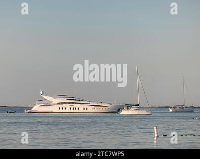 Grande yacht a motore e due barche a vela all'ancora Foto Stock