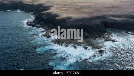 Vista aerea di una costa desertica con onde turchesi che si infrangono sulla riva dell'isola di fuerteventura in spagna Foto Stock