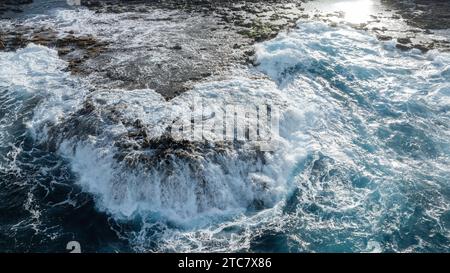 Onde del mare schiumose che si infrangono sulla costa rocciosa con la luce del sole che si riflette sull'acqua dell'isola di fuerteventura Foto Stock