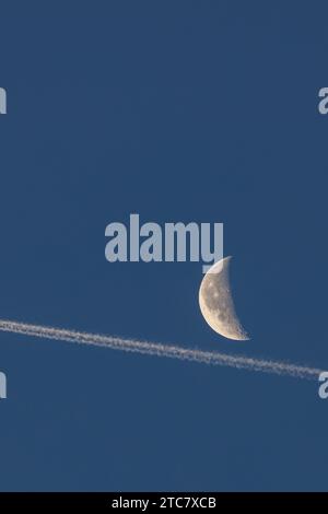 Una splendida immagine di una mezza luna e di un luminoso sentiero di condensazione all'alba in una chiara mattinata d'inverno nel Regno Unito Foto Stock