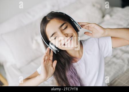 Una ragazza pre-adolescente ascolta la musica attraverso le cuffie wireless, con vista ravvicinata del volto. Utilizzo della tecnologia moderna, divertimento, tempo libero Foto Stock