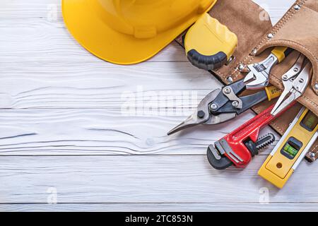 Set di utensili da costruzione nella cintura portautensili elmetto su tavola di legno Foto Stock