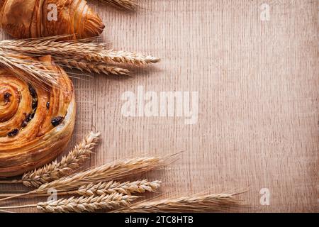 Brioche dolci alle orecchie di grano dorato con uvetta su tavola di legno e bevande Foto Stock