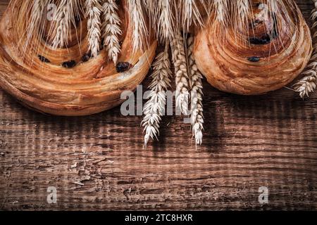 Un mucchio di orecchie di grano, panetteria dolce con uva passa su un concetto di cibo e bevande in legno di quercia Foto Stock