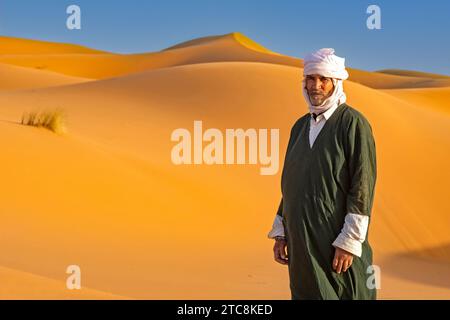 Uomo berbero marocchino che indossa kaftan e turbante nelle dune di sabbia di Erg Chebbi nel deserto del Sahara vicino a Merzouga, Drâa-Tafilalet, Errachidia, Marocco Foto Stock