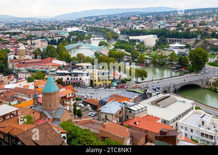 Tbilisi, Georgia - 23 settembre 2023: Vista dall'alto della città di Tbilisi con il ponte Metechi e il Rike Park dalla fortezza di Narikala su nuvoloso evenig autunnale Foto Stock