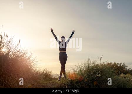donna sportiva con le braccia alzate che celebra gli obiettivi dopo l'allenamento sportivo e che si allena all'aperto dopo una corsa mattutina Foto Stock