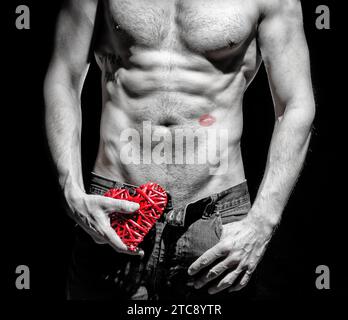 Uomo atletico di giorno felice valentine con cuore rosso decorativo su sfondo scuro Foto Stock