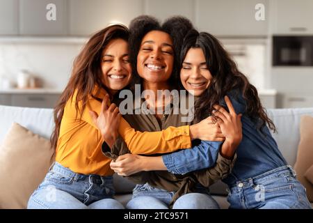 Tre diverse amiche che si abbracciano sedute sul divano all'interno di casa Foto Stock