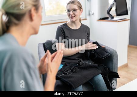 Donna in possesso di un giubbotto da addestramento EMS per spiegare al cliente la funzione che le parla in una sala di consulenza Foto Stock