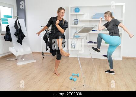 Cliente e allenatore che fanno esercizi al ginocchio in palestra, uno che indossa una suite di allenamento EMS in palestra. Foto Stock