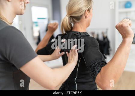 Trainer che aiuta una donna a regolare un costume da allenamento EMS in palestra Foto Stock