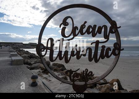 "Silhouette di un cartello circolare con il testo "Oceano Atlantico" su un cielo nuvoloso e sullo sfondo della spiaggia." Foto Stock