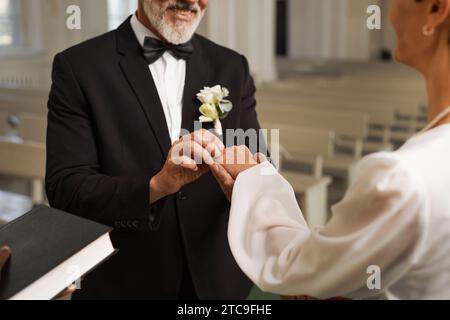 Primo piano dello sposo anziano che si scambia anelli con la sposa durante la cerimonia di nozze in chiesa Foto Stock