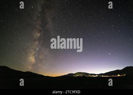 La via Lattea Galaxy che si innalza sopra i sentieri leggeri a sinistra di un'auto che viaggia sull'autostrada 20. Craters of the Moon National Monument, Idaho Foto Stock