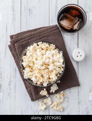 Popcorn su una ciotola con sale sopra e tavolo di legno di soda. Foto Stock