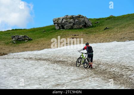 Mountain Biker spinge la sua Mountain Bike su Un campo di neve, Montriond, Chablais, Francia Foto Stock