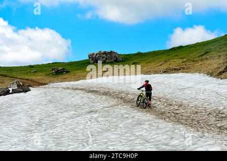 Mountain Biker spinge la sua Mountain Bike su Un campo di neve, Montriond, Chablais, Francia Foto Stock