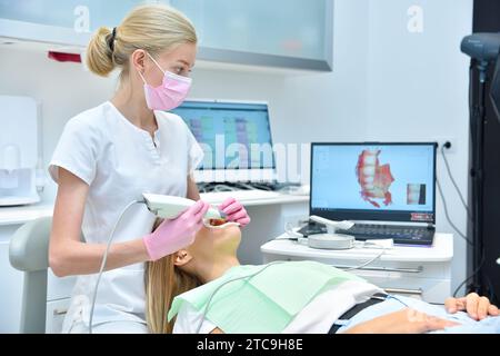 Paziente con scing ortodontista con scanner intraorale dentale e processo di controllo sullo schermo del laptop. Concetto di protesi e stomatologia. Foto Stock