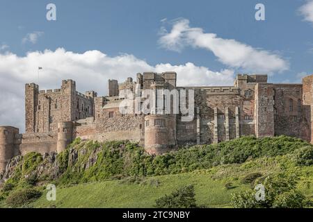 North Yorkshire, Bamburgh - 26 giugno 2023 - guardando su un pendio erboso di un castello su una collina con una bandiera che sventola Foto Stock