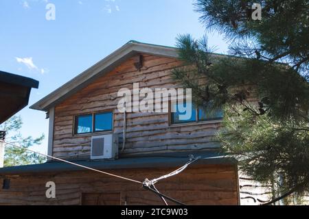 Una pittoresca cabina di legno nel mezzo di un campo, caratterizzata da un'antenna esterna, un computer portatile aperto sul davanzale e diverse finestre Foto Stock