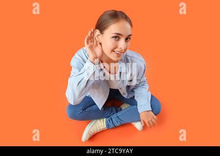 Ragazza adolescente che cerca di sentire qualcosa su sfondo arancione Foto Stock