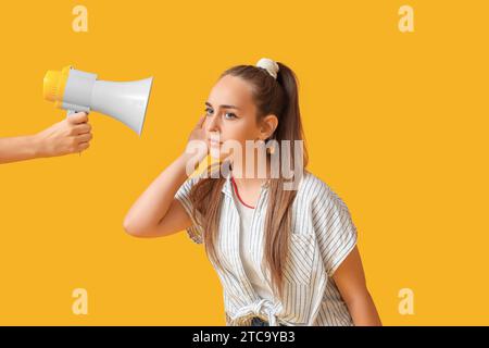 Ragazza adolescente che cerca di sentire qualcosa e mano con il megafono su sfondo giallo Foto Stock