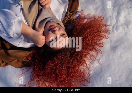 Vista dall'alto di una donna grassa dai capelli rossi sdraiata sulla neve. Foto Stock