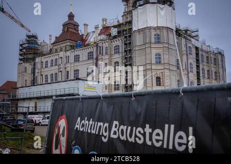 PRODUZIONE - 11 dicembre 2023, Meclemburgo-Pomerania occidentale, Güstrow: Davanti al castello è appeso un cartello con la scritta "attenzione cantiere", completamente impalcato e coperto con teli stampati per lavori di ristrutturazione. Il castello di Güstrow è considerato uno dei più importanti edifici rinascimentali della Germania settentrionale. Il guscio esterno del castello rinascimentale di Güstrow è stato ampiamente ristrutturato al costo di molti milioni di euro. I documenti storici e le foto degli archivi della città di Güstrow forniscono informazioni sulla storia della ristrutturazione del XVI secolo Foto Stock