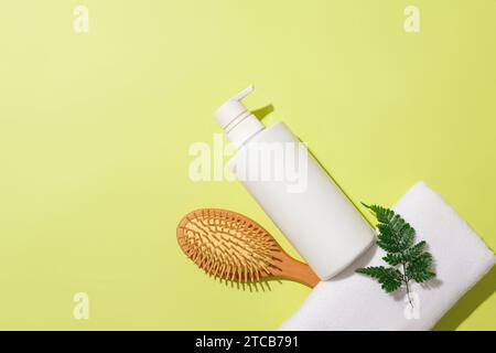 Una bottiglia di gel doccia non etichettata, un pettine per sbattere, un asciugamano e foglie di felce sono visualizzati su uno sfondo pastello. Prodotti per la cura del corpo. Mockup cosmetico f Foto Stock