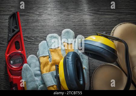 Set di protezione per l'udito guanti di sicurezza stivali in pelle impermeabili livello di costruzione su tavola di legno Foto Stock