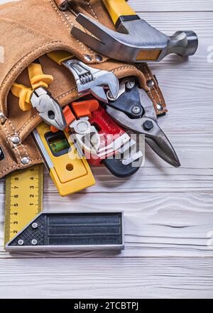 Cintura portautensili in pelle marrone con attrezzi da costruzione su un asse di legno direttamente sopra di essa Foto Stock