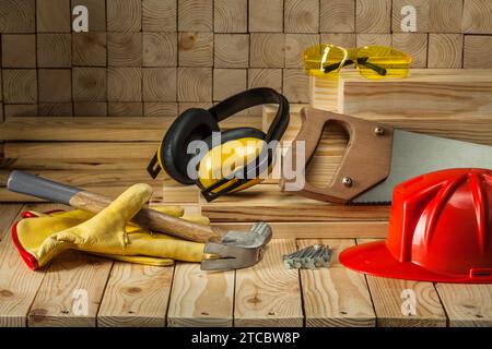 Carpenter's tools guanti casco occhiali di sicurezza martello sega a mano cuffie unghie sega a mano su sfondo di legno Foto Stock