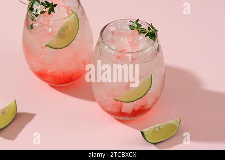 Cocktail a base di frutti di bosco con ghiaccio tritato, lime e timo su sfondo rosa Foto Stock