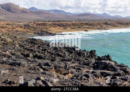 Vista panoramica sulla costa di El Cotillo sull'isola canaria di Fuerteventura, Spagna con rocce laviche e catena montuosa sullo sfondo Foto Stock